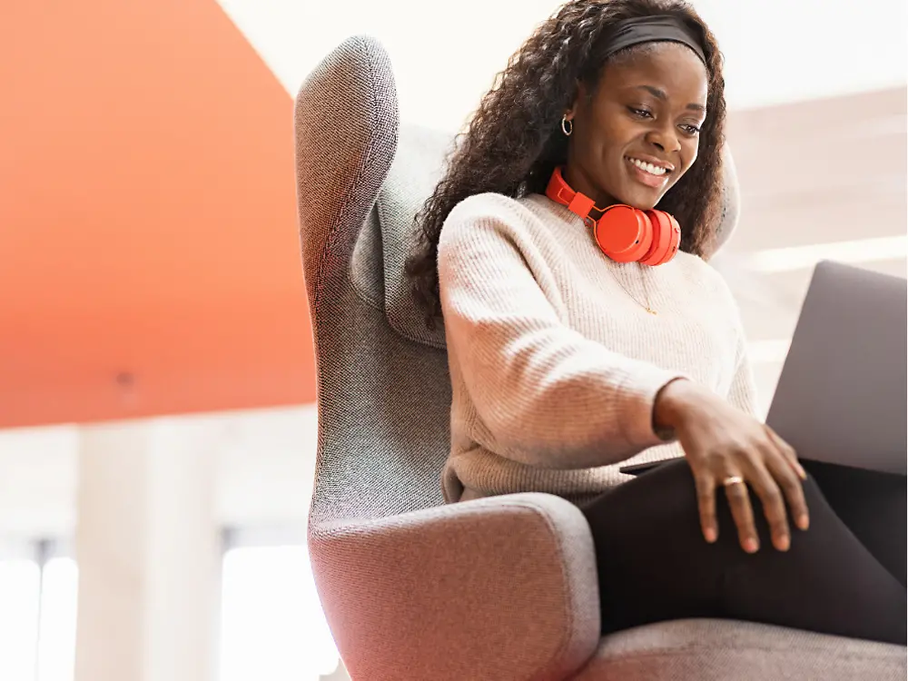 Una empleada de Henkel se sienta en una silla cómoda con su computadora portátil sobre las rodillas. Ella sonríe. 