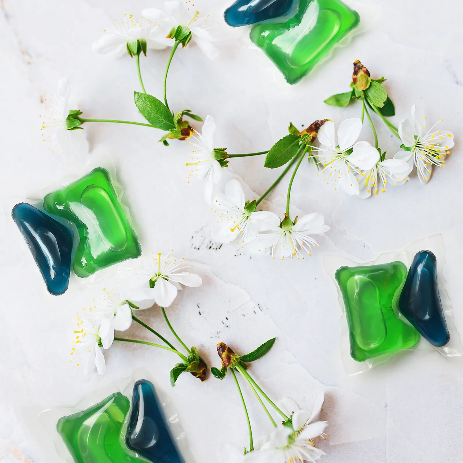 Dos cápsulas verdes y azules de Henkel Persil con flores de cerezo alrededor