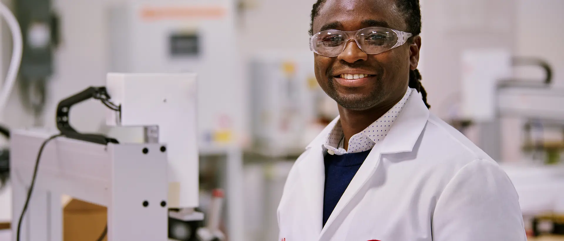 Persona con una bata blanca de laboratorio de Henkel, de pie en un entorno de laboratorio rodeado de equipos y maquinaria